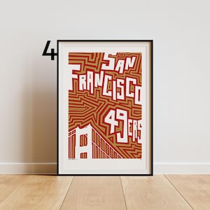 May include: Framed art print with the words "SAN FRANCISCO 49ERS" in white, set against a red and gold background. The Golden Gate Bridge is illustrated at the bottom. The print is in a black frame.