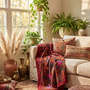May include: A living room with a cream sofa, patterned cushions, and a red throw. Decorative vases hold pampas grass, and potted plants add greenery. The room is bright with natural light, creating a warm and inviting atmosphere.