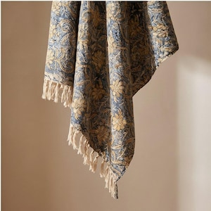 Peut inclure: Un jeté de lit en tissu tissé présentant un motif dense et répétitif de fleurs et de vignes dans des tons de bleu sourd et de beige doré. Le tissu a un aspect texturé et est fini avec de longues franges de couleur crème sur les bords inférieurs.