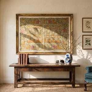 May include: A rectangular wooden console table with a dark brown finish, featuring a large framed textile wall hanging with animal motifs, a row of five books, two small elephant figurines, and a white vase with blue brushstroke patterns.