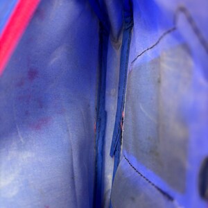 Op de afbeelding: Binnenaanzicht van een blauwe tas met een roze rits. De binnenkant is lichtblauw, met zichtbare stiksels en wat vlekken. De roze rits vormt een helder contrast met de blauwe stof.