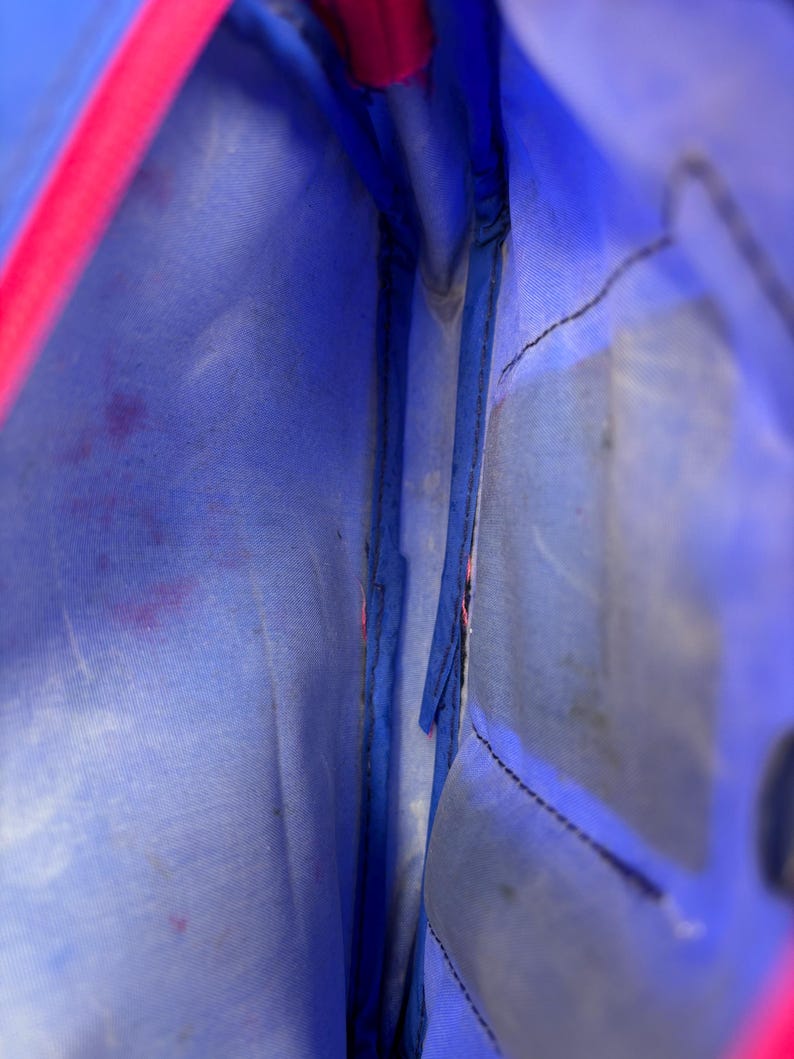 Op de afbeelding: Binnenaanzicht van een blauwe tas met een roze rits. De binnenkant is lichtblauw, met zichtbare stiksels en wat vlekken. De roze rits vormt een helder contrast met de blauwe stof.