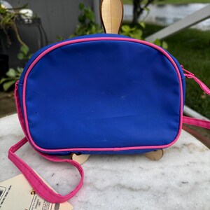 Op de afbeelding: Een blauwe handtas met roze rand en riem, met een houten schildpadontwerp. De tas heeft een afgeronde vorm en een roze riem. Een klein Ariel-beeldje is rechtsonder zichtbaar.