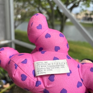 Pu&ograve; includere: Un peluche rosa con motivi a cuore viola. Il giocattolo ha un'etichetta che recita "MATTEL, INC. ARCOTOYS, INC. 2769 CB, MADE IN CHINA, &copy;Disney". &Egrave; un prodotto Disney.