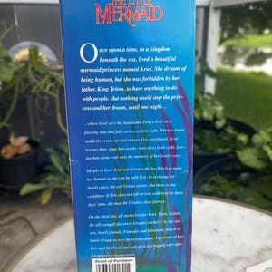 Pode incluir: Uma caixa retangular azul de papel&atilde;o para um brinquedo Disney A Pequena Sereia. A frente apresenta o t&iacute;tulo do filme em texto vermelho, um resumo da hist&oacute;ria, ilustra&ccedil;&otilde;es de algas roxas, um logotipo Tyco e um c&oacute;digo de barras com o texto Proof-of-Purchase.