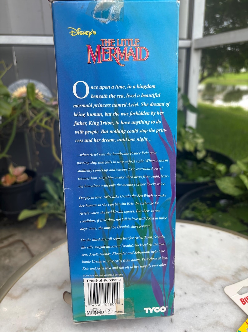 Pode incluir: Uma caixa retangular azul de papel&atilde;o para um brinquedo Disney A Pequena Sereia. A frente apresenta o t&iacute;tulo do filme em texto vermelho, um resumo da hist&oacute;ria, ilustra&ccedil;&otilde;es de algas roxas, um logotipo Tyco e um c&oacute;digo de barras com o texto Proof-of-Purchase.