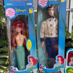 May include: Two vintage Disney's The Little Mermaid dolls in their original boxes. One doll is Ariel, with red hair and a green tail. The other is Prince Eric, in a white jacket and blue pants. The boxes feature Disney's branding and the text "From Disney's Award-winning Movie!"