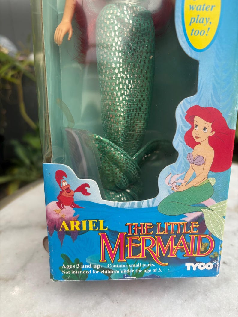 Pode incluir: Uma boneca Ariel A Pequena Sereia da Tyco na embalagem original. A caixa apresenta um gr&aacute;fico da Ariel e do Sebasti&atilde;o, com o texto Ariel The Little Mermaid, water play, too!, e Ages 3 and up. Contains small parts.