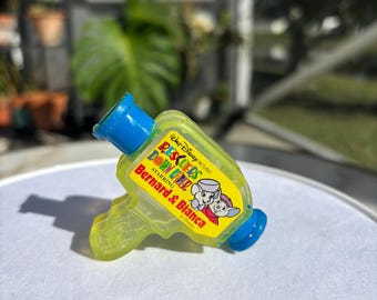 May include: A vintage, yellow and blue toy water gun featuring the text "Rescuers Down Under" and the characters Bernard and Bianca. The toy is made of translucent plastic and has a blue nozzle and handle.