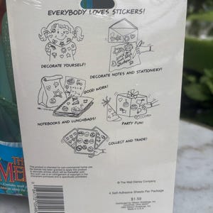 Pode incluir: Um suporte de cart&atilde;o retangular para um conjunto de autocolantes com ilustra&ccedil;&otilde;es de linhas a preto e branco que mostram v&aacute;rias formas de usar autocolantes. O texto diz EVERYBODY LOVES STICKERS, DECORATE YOURSELF, DECORATE NOTES AND STATIONERY, GOOD WORK, NOTEBOOKS AND LUNCHBAGS, PARTY FUN e COLLECT AND TRADE. Um c&oacute;digo de barras e informa&ccedil;&otilde;es de direitos de autor est&atilde;o impressos na parte inferior.