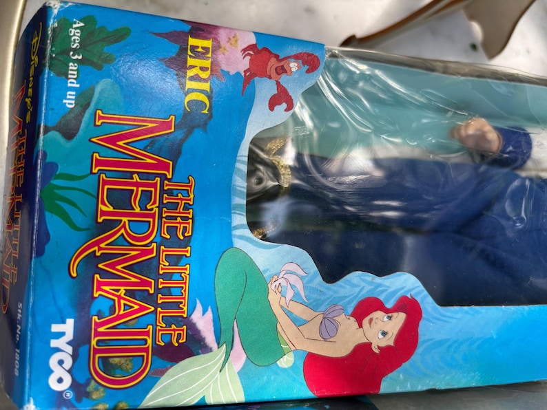May include: A vintage "The Little Mermaid" toy box featuring Ariel, Eric, and Sebastian. The box is blue with colorful graphics and the Tyco logo. The toy is for ages 3 and up.