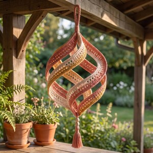 May include: A hanging crochet ornament featuring a spiraling, open-work design in a gradient of peach, yellow, and cream yarn. The structure is suspended by a braided loop at the top and finished with a small tassel and wooden beads at the bottom.