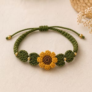 May include: A handmade green crochet bracelet featuring a yellow and brown sunflower in the center. The bracelet has green leaves and gold beads. The adjustable closure allows for a comfortable fit.