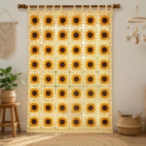 Könnte beinhalten: Ein gehäkelter Vorhang mit einem sich wiederholenden Sonnenblumenmuster. Die Sonnenblumen haben gelbe Blütenblätter und dunkelbraune Zentren, vor einem cremefarbenen Hintergrund. Der Vorhang hängt an einer Holzstange.