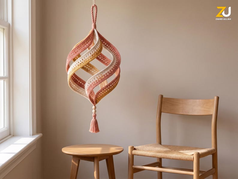 May include: A hanging spiral ornament crafted from crocheted yarn in shades of dusty rose, mustard yellow, and cream. The structure features a twisted, open-work design with a braided loop at the top and a decorative wooden bead and tassel at the bottom.