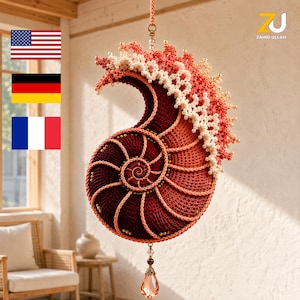 May include: A hanging crochet nautilus shell ornament in shades of deep red, orange, and cream. The shell features intricate spiral stitching, small gold beads, and a cream-coloured lace-like crest. A faceted amber-coloured crystal hangs from the bottom.