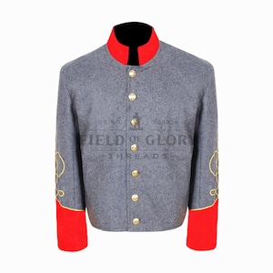 Op de afbeelding: Een grijze militaire jas met een rode kraag en manchetten, gouden knopen en geborduurde details op de mouwen. De jas heeft de tekst "FIELD OF GLORY THREADS" erop.