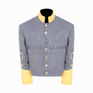 May include: A gray military jacket with a yellow collar and cuffs. The jacket has gold buttons and yellow decorative accents on the sleeves. The text "FIELD OF GLORY THREADS" is printed on the front.