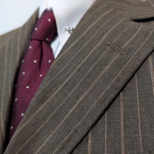 May include: Close-up of a brown pinstripe suit jacket with a white dress shirt and a burgundy tie with white polka dots. The suit jacket has a notched lapel and a small buttonhole.