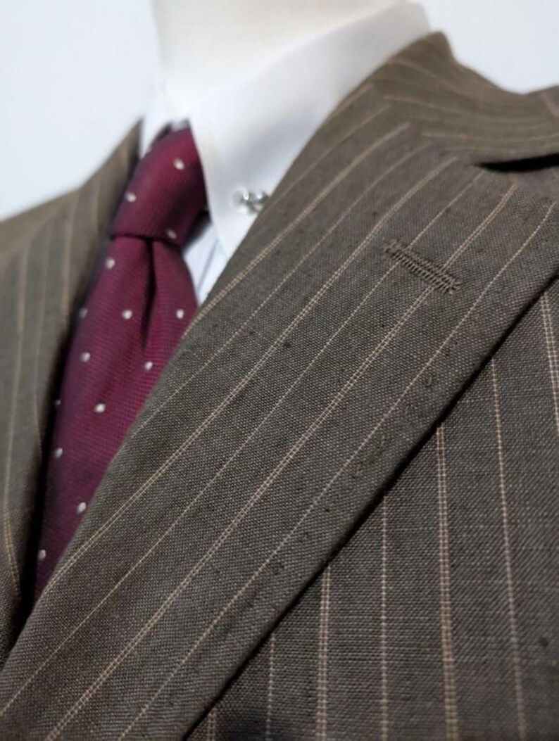 May include: Close-up of a brown pinstripe suit jacket with a white dress shirt and a burgundy tie with white polka dots. The suit jacket has a notched lapel and a small buttonhole.