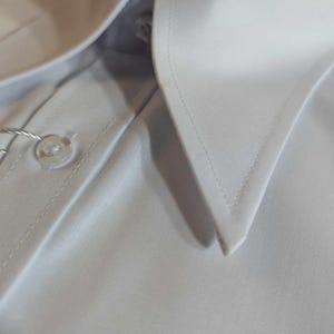 Puede incluir: Una camisa blanca de vestir con cuello abotonado y un solo bot&oacute;n de cierre.