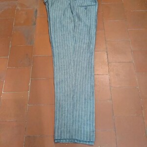 Może przedstawiać: Szare i białe spodnie w paski. Spodnie wykonane są z lekkiego materiału i mają klasyczny kr&oacute;j z zapięciem na guziki i zamek błyskawiczny. Spodnie są starannie złożone na kafelkowanej powierzchni.