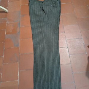 May include: Dark olive green dress pants with vertical white pinstripes. The pants are laid flat on a tiled surface. The pants have a button and zipper closure and two back pockets.