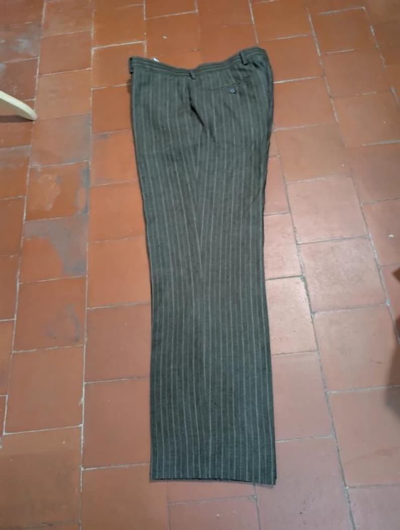 May include: Dark olive green dress pants with vertical white pinstripes. The pants are laid flat on a tiled surface. The pants have a button and zipper closure and two back pockets.