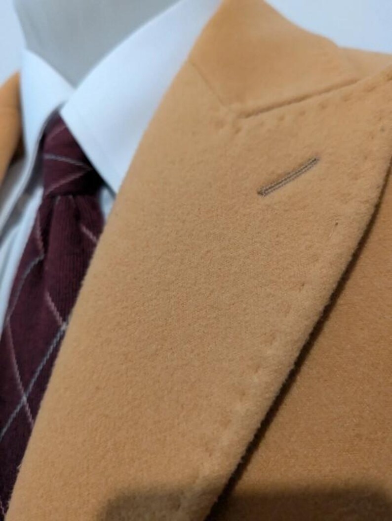 Puede incluir: Primer plano de una blazer color beige con una camisa blanca con cuello y una corbata a cuadros burdeos. La blazer tiene un ojal y una tela texturizada. La corbata presenta un patr&oacute;n de cuadros cl&aacute;sico.