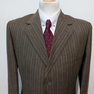 May include: Brown pinstripe suit jacket with a white dress shirt and a burgundy polka dot tie. The suit is displayed on a mannequin. The jacket has a two-button closure and a chest pocket.