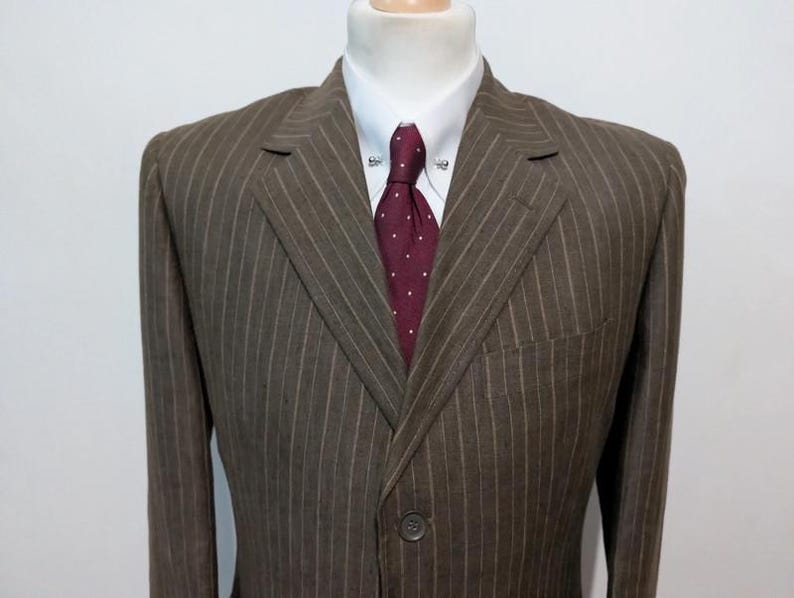 May include: Brown pinstripe suit jacket with a white dress shirt and a burgundy polka dot tie. The suit is displayed on a mannequin. The jacket has a two-button closure and a chest pocket.