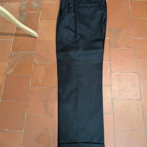 Puede incluir: Pantalones de vestir gris oscuro con dobladillo vuelto. Los pantalones tienen cierre de bot&oacute;n y trabillas para el cintur&oacute;n. La tela tiene un sutil patr&oacute;n de rayas verticales. Los pantalones est&aacute;n doblados cuidadosamente sobre una superficie embaldosada.