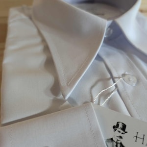 Puede incluir: Camisa blanca de vestir con cuello abotonado y pu&ntilde;o de un bot&oacute;n. La camisa tiene una etiqueta con un logotipo de un hombre con un sombrero de copa.