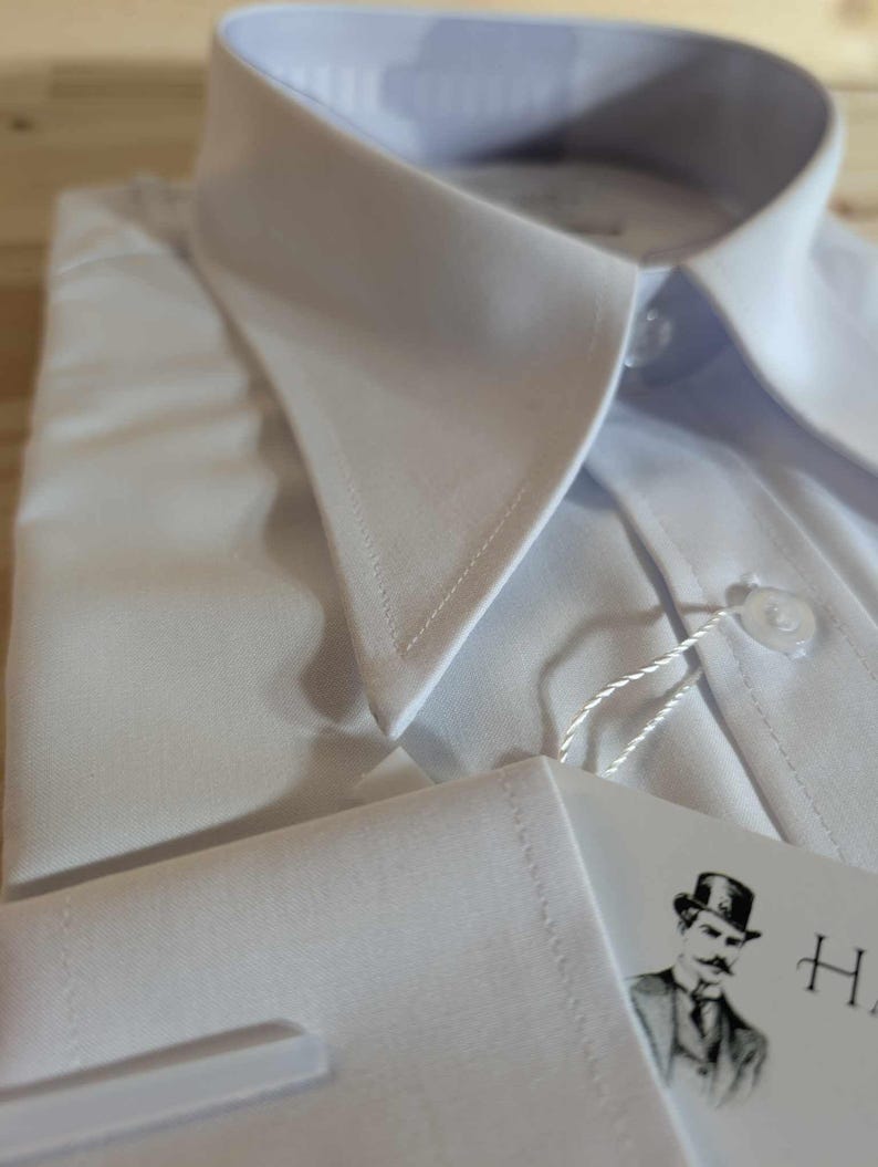 Puede incluir: Camisa blanca de vestir con cuello abotonado y pu&ntilde;o de un bot&oacute;n. La camisa tiene una etiqueta con un logotipo de un hombre con un sombrero de copa.