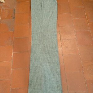 May include: A pair of gray, vertically striped trousers. The pants have a high waist and a flared leg. The fabric appears to be a medium-weight material, suitable for cooler weather. The trousers are laid flat on a tiled surface.