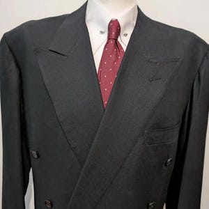 May include: A black double-breasted suit jacket with a white dress shirt and a burgundy tie with white polka dots. The jacket has a notched lapel and a pocket on the left side. The suit is displayed on a mannequin.