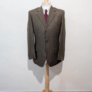 May include: A brown pinstripe blazer with a white dress shirt and a burgundy polka dot tie. The three-button blazer is displayed on a wooden mannequin. The blazer has two front pockets and three buttons on each sleeve.