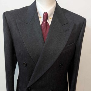 Puede incluir: Chaqueta de traje cruzada gris carb&oacute;n, camisa blanca y corbata burdeos con lunares blancos. La chaqueta tiene solapa de muesca y dos filas de botones. Ropa formal.