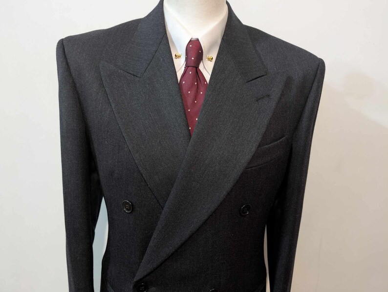 Puede incluir: Chaqueta de traje cruzada gris carb&oacute;n, camisa blanca y corbata burdeos con lunares blancos. La chaqueta tiene solapa de muesca y dos filas de botones. Ropa formal.