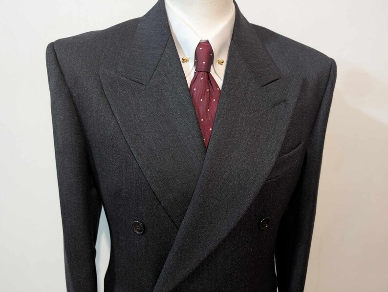 Puede incluir: Chaqueta de traje cruzada gris carb&oacute;n con camisa blanca de cuello y corbata burdeos con lunares blancos. La chaqueta tiene dos filas de botones y solapa con muescas.