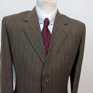 May include: A brown pinstripe suit jacket with a white dress shirt and a burgundy tie with white polka dots. The suit has a single-button closure and a notched lapel. The tie has a tie pin.