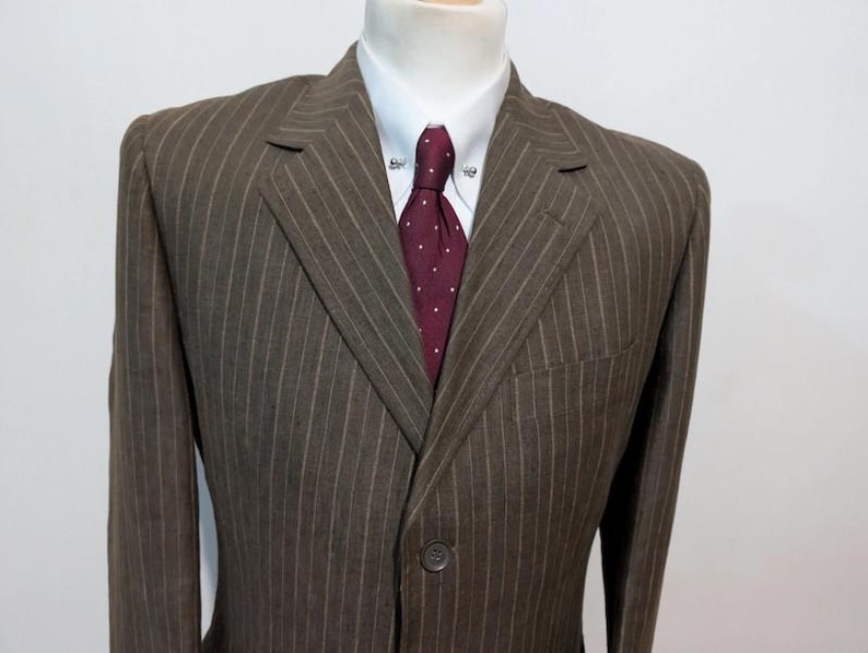 May include: A brown pinstripe suit jacket with a white dress shirt and a burgundy tie with white polka dots. The suit has a single-button closure and a notched lapel. The tie has a tie pin.