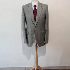 May include: A gray pinstripe blazer with a white collared shirt and a burgundy tie. The blazer has two front pockets and a single button closure. The outfit is displayed on a wooden mannequin.