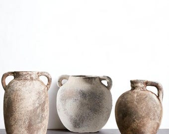 May include: Three antique-style ceramic vases in varying shapes and sizes. The vases have a textured, aged appearance with shades of brown, beige, and gray. Each vase features two loop handles on the sides, adding to their rustic charm.