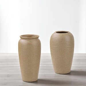 May include: Two beige ceramic vases with a textured, ribbed design. The vases have a neutral color and a simple, elegant shape. One vase is taller and more cylindrical, while the other is shorter and more rounded. They are suitable for home decor.