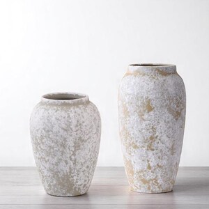 May include: Two decorative vases with a textured, aged appearance. The vases are off-white with tan and gray accents, creating a rustic aesthetic. The taller vase is approximately 18 inches tall, while the shorter one is about 12 inches.