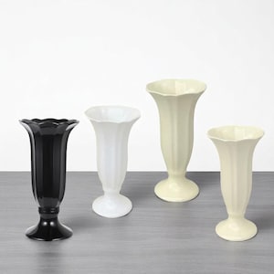 May include: Four ceramic vases in a row, each with a fluted design and a flared top. The vases are in black, white, and two shades of cream. The vases have a pedestal base and are suitable for displaying flowers.