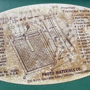 May include: A close-up of a beige oval sticker with a diagram of a trimmer and a list of parts. The sticker is labeled "Premier Trimmer Parts" and includes instructions for using the trimmer. The sticker is on a green surface.