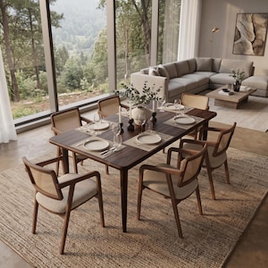 May include: A rectangular dark wood dining table with rounded corners, surrounded by six wooden chairs featuring woven cane backrests and light beige upholstered seats. The table is set with white plates, glassware, and candles in a bright room.