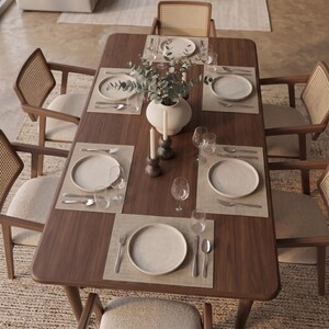 May include: A rectangular dark wood dining table set for six with light-colored placemats, white ceramic plates, stainless steel silverware, clear glassware, two dark gray candle holders with white taper candles, and a central white vase.
